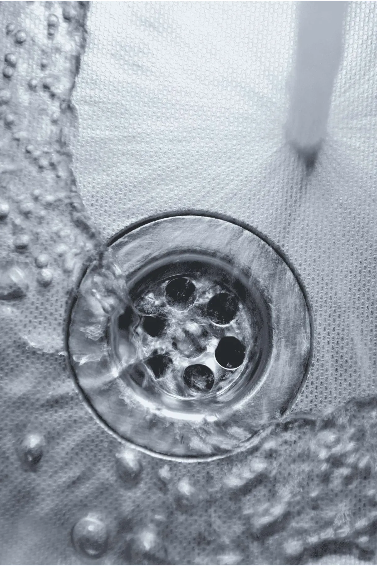 Close-up view of water flowing into a drain with bubbles and ripples in a textured sink surface.