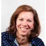 Smiling woman with curly brown hair wearing blue polka dot shirt against a white background