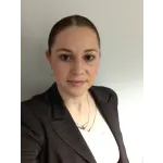 Professional woman with light skin, pulled-back hair, black blazer, white top, and silver necklace on plain background.