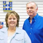 Smiling middle-aged man and woman standing together in a store with products on display behind them