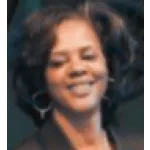 Smiling woman with curly hair wearing hoop earrings against a dark background