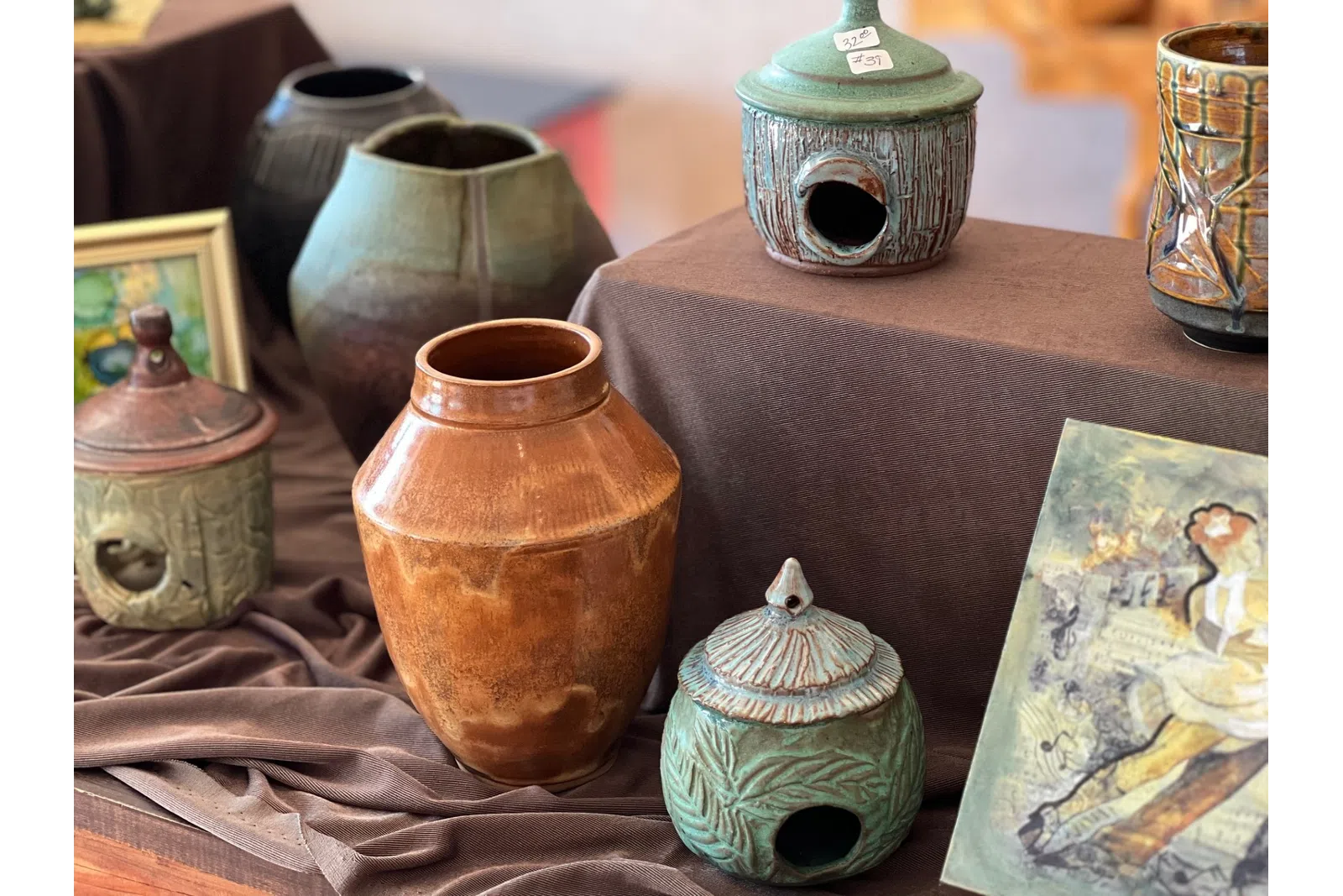 Assorted handcrafted ceramic pots and decorative jars displayed on brown fabric at an art market.