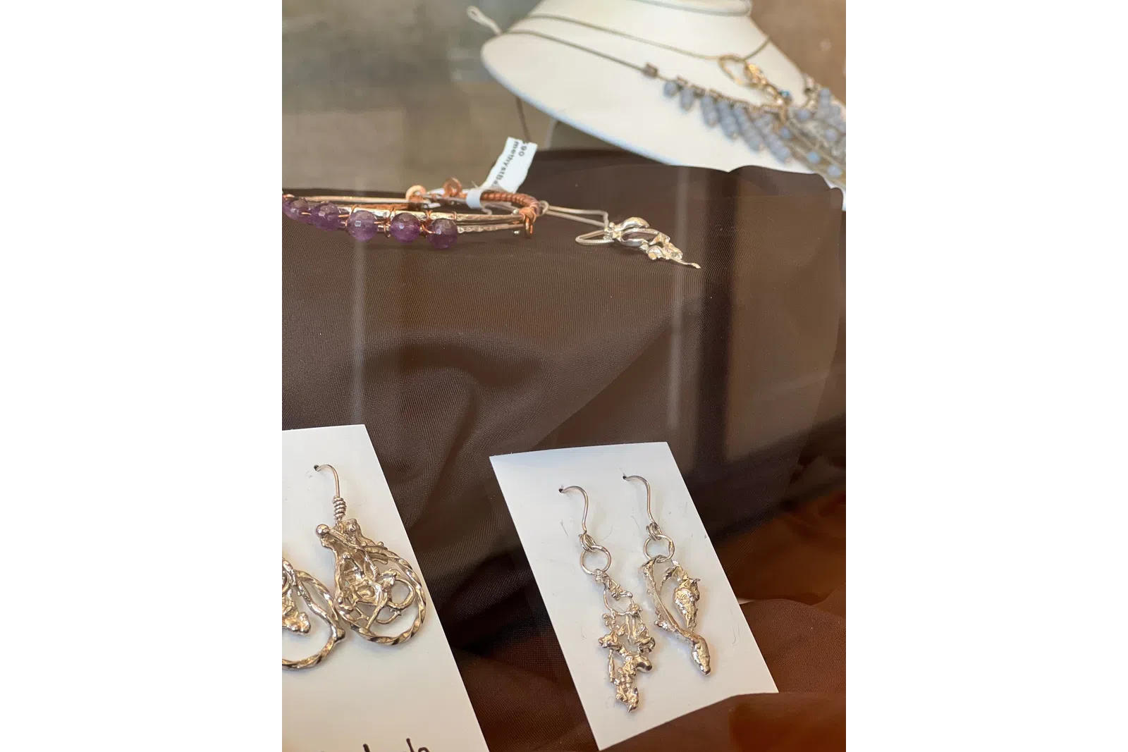Display of handcrafted silver earrings and beaded bracelets on brown fabric in a jewelry showcase.