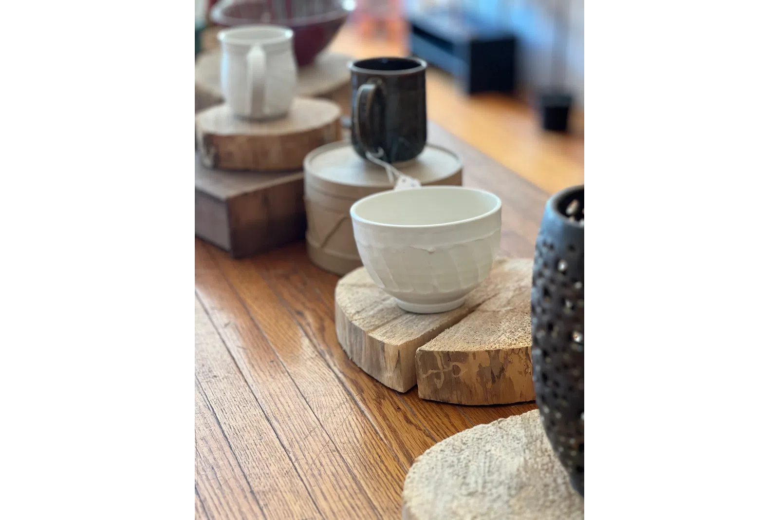 White and black ceramic cups on rustic wooden coasters arranged on a wooden table with natural light.