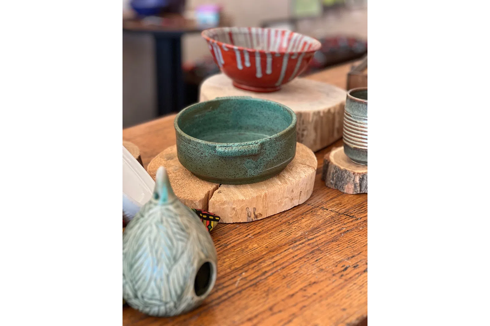 Various handcrafted ceramic bowls and vessels displayed on wooden slices on a rustic wooden table.