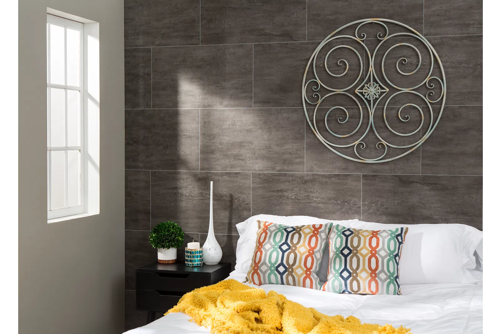 Cozy bedroom with patterned pillows, yellow throw blanket, decorative wall art, and natural light from window