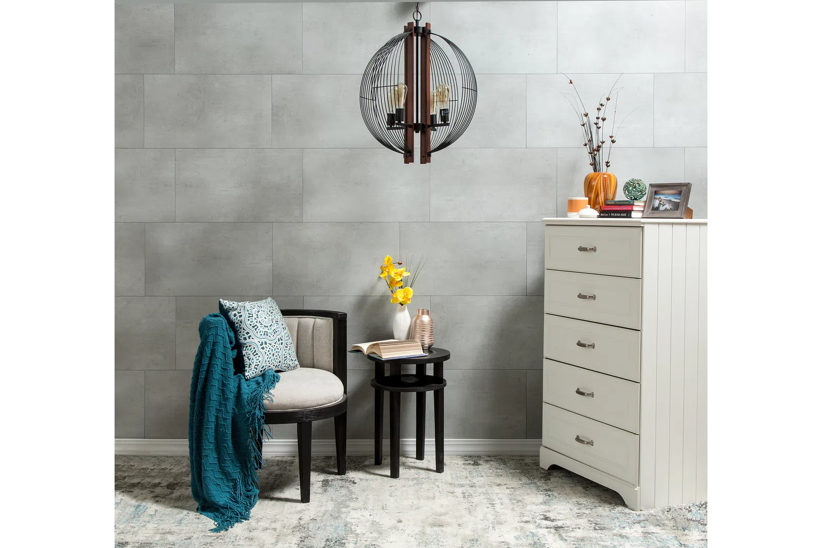 Cozy reading corner with armchair, teal throw, side tables, flowers, and white dresser against gray wall.