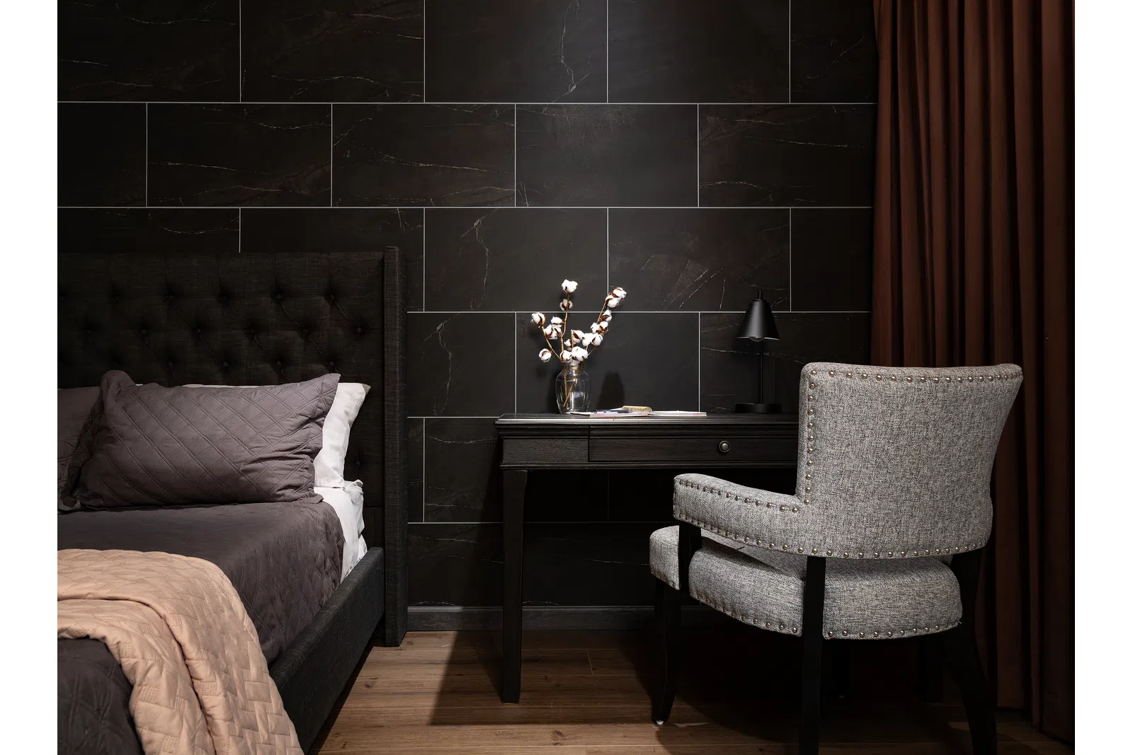 Modern bedroom corner with dark tiled wall, upholstered bed, black desk, gray chair, and brown curtains.