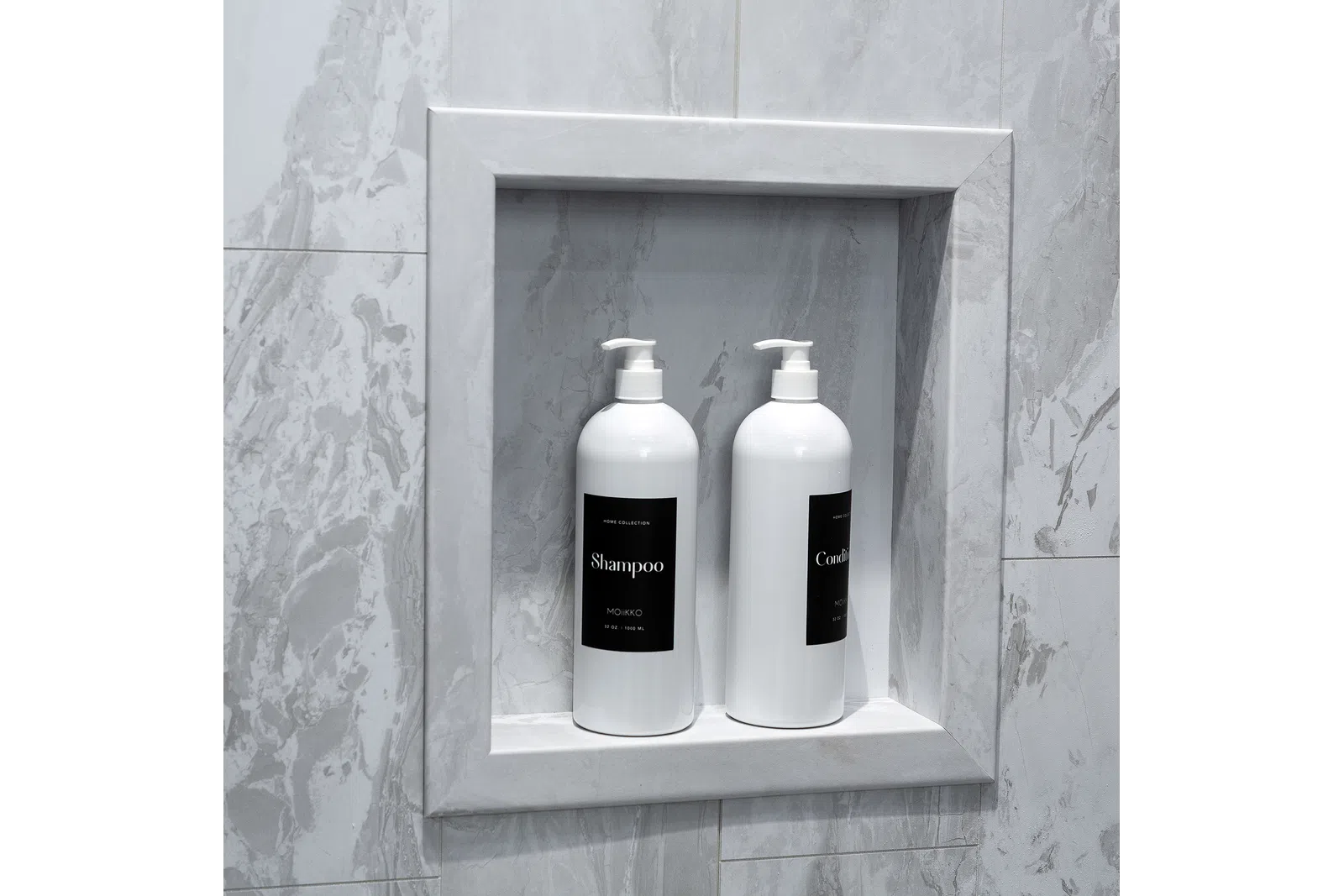 Two white pump bottles of shampoo and conditioner in a recessed marble shower niche.