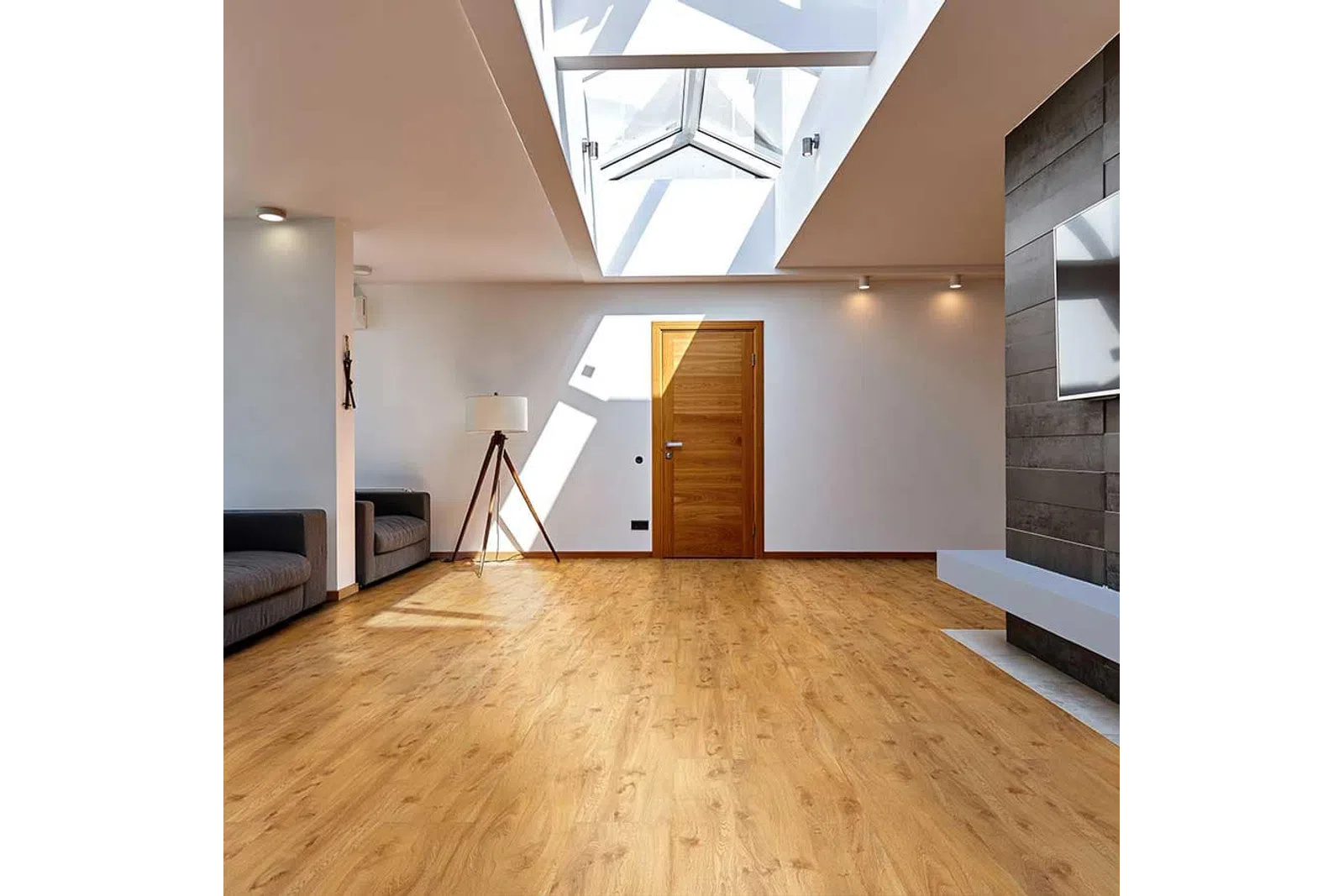 Bright modern living room with wooden flooring, skylight, wooden door, gray sofas, and a tripod floor lamp.