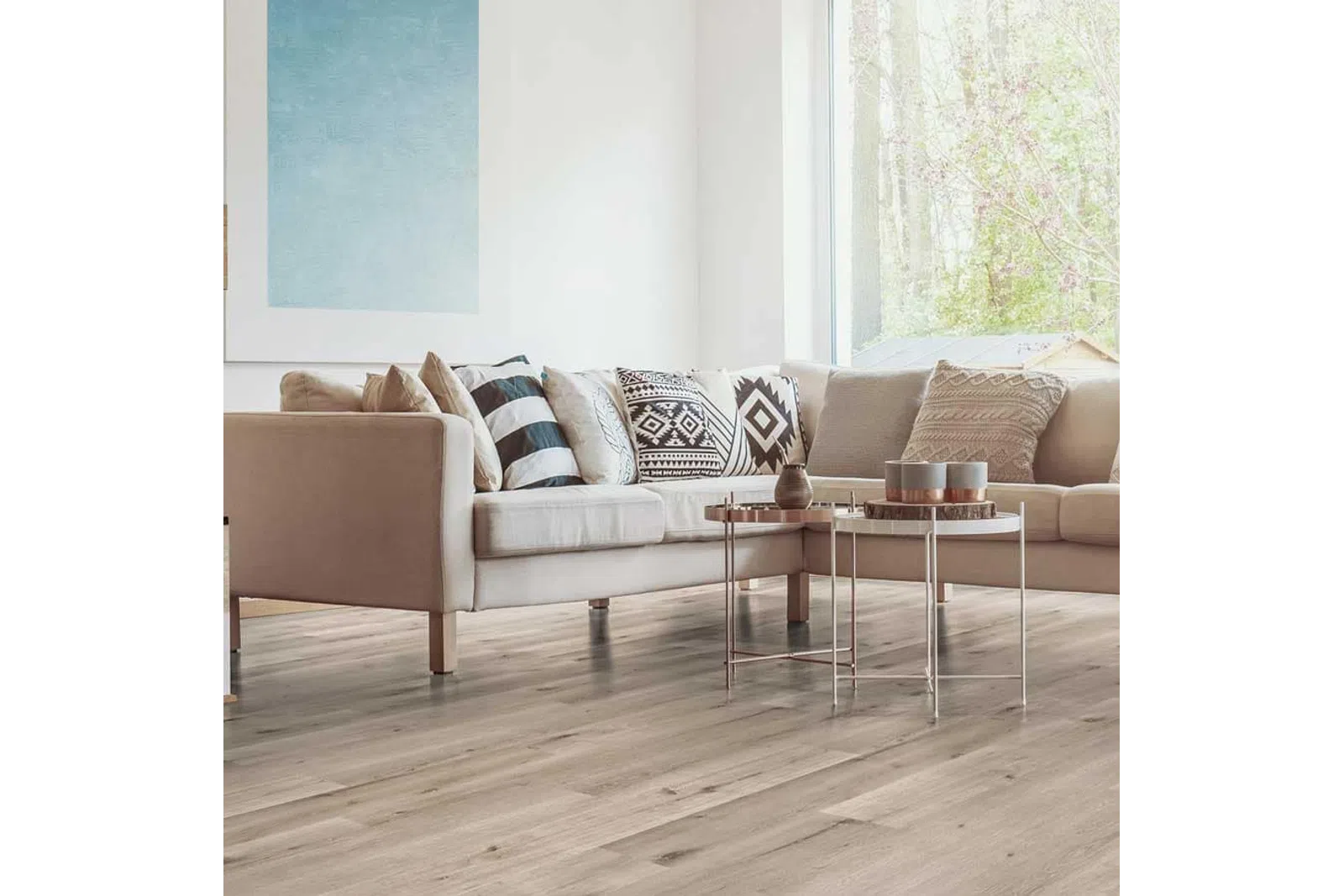 Modern living room with beige sectional sofa, patterned cushions, wooden floor, and two round metal coffee tables.