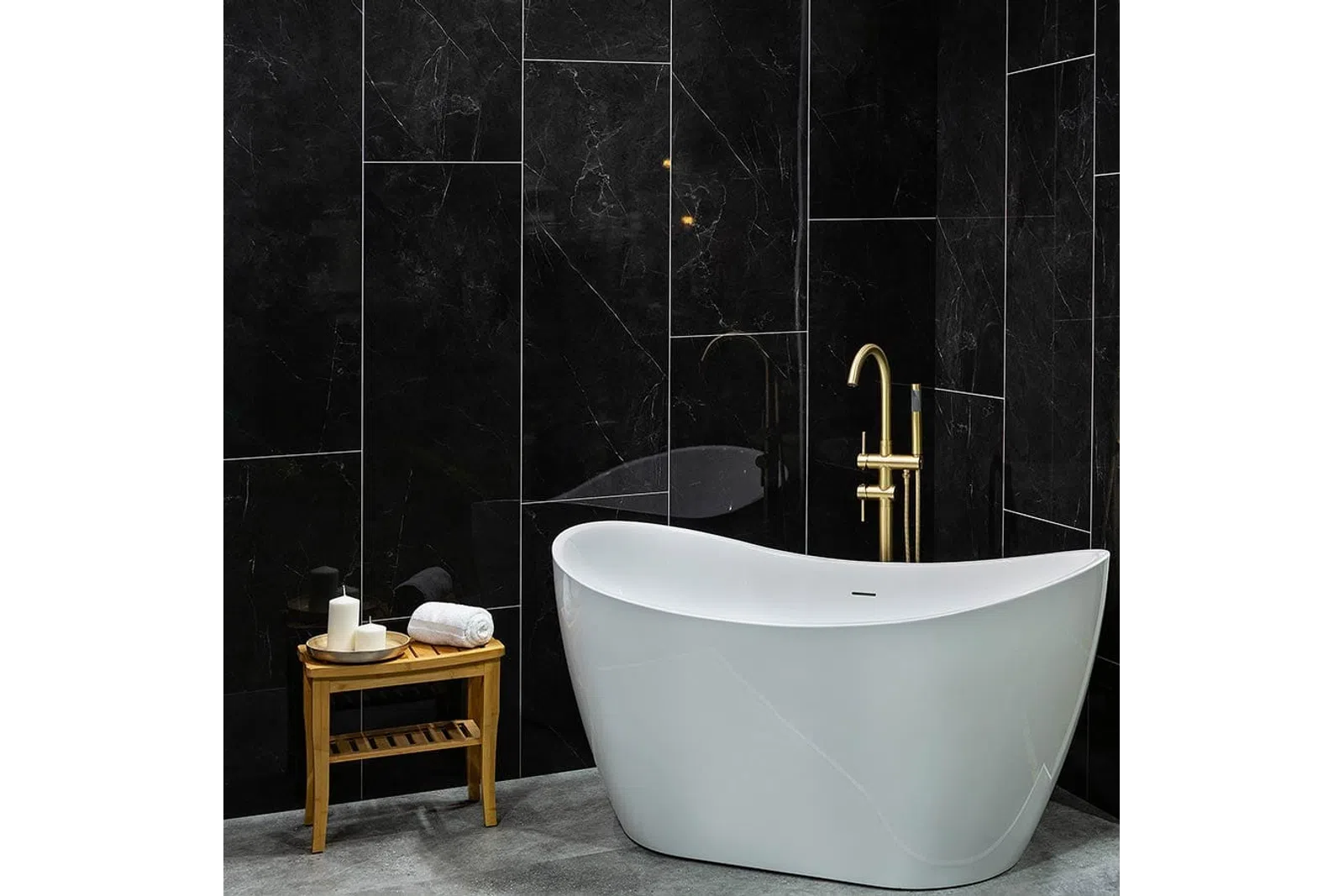 Modern white freestanding bathtub with gold faucet against sleek black marble wall with wooden side table.