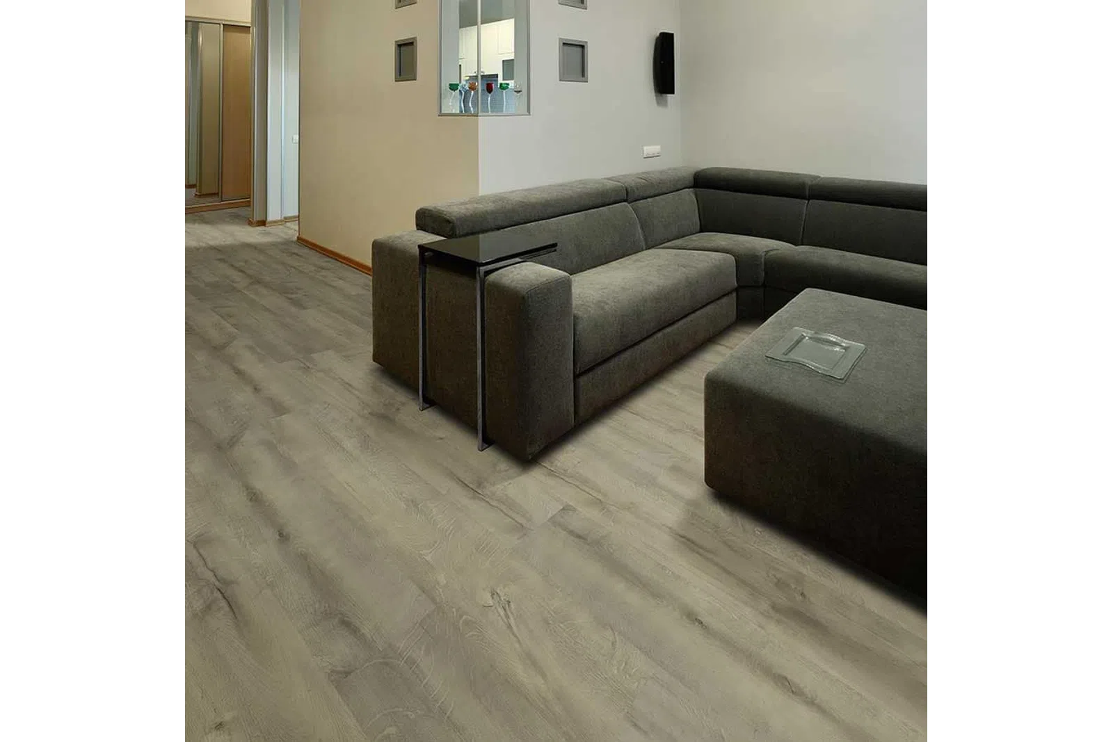 Modern living room with gray sectional sofa, dark ottoman, and light wood laminate flooring under soft lighting.
