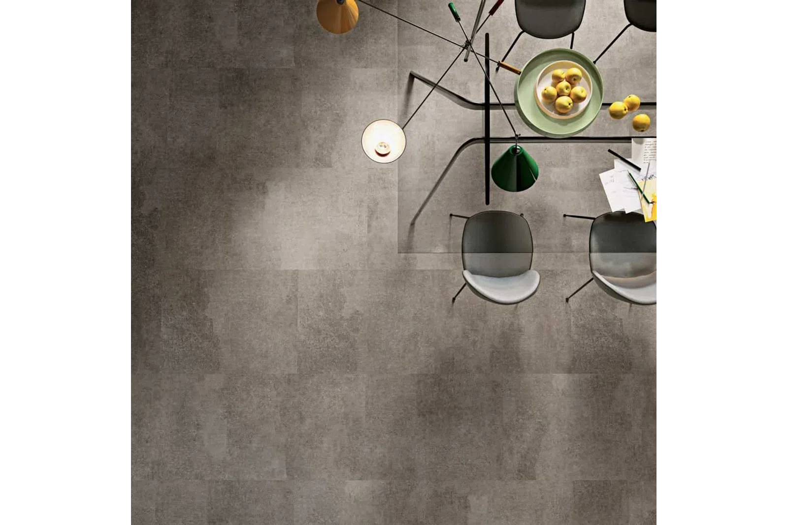 Top view of modern glass dining table with chairs, pendant lights, a bowl of lemons, and scattered papers.
