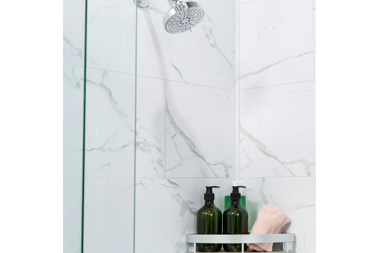 Modern showerhead with glass shower screen, marble wall tiles, green soap dispensers, and a folded towel on a rack.