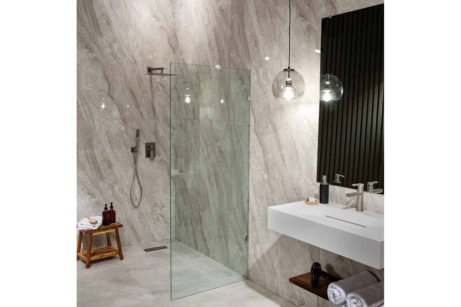 Modern bathroom with glass shower enclosure, marble walls, floating sink, pendant light, and wooden stools.