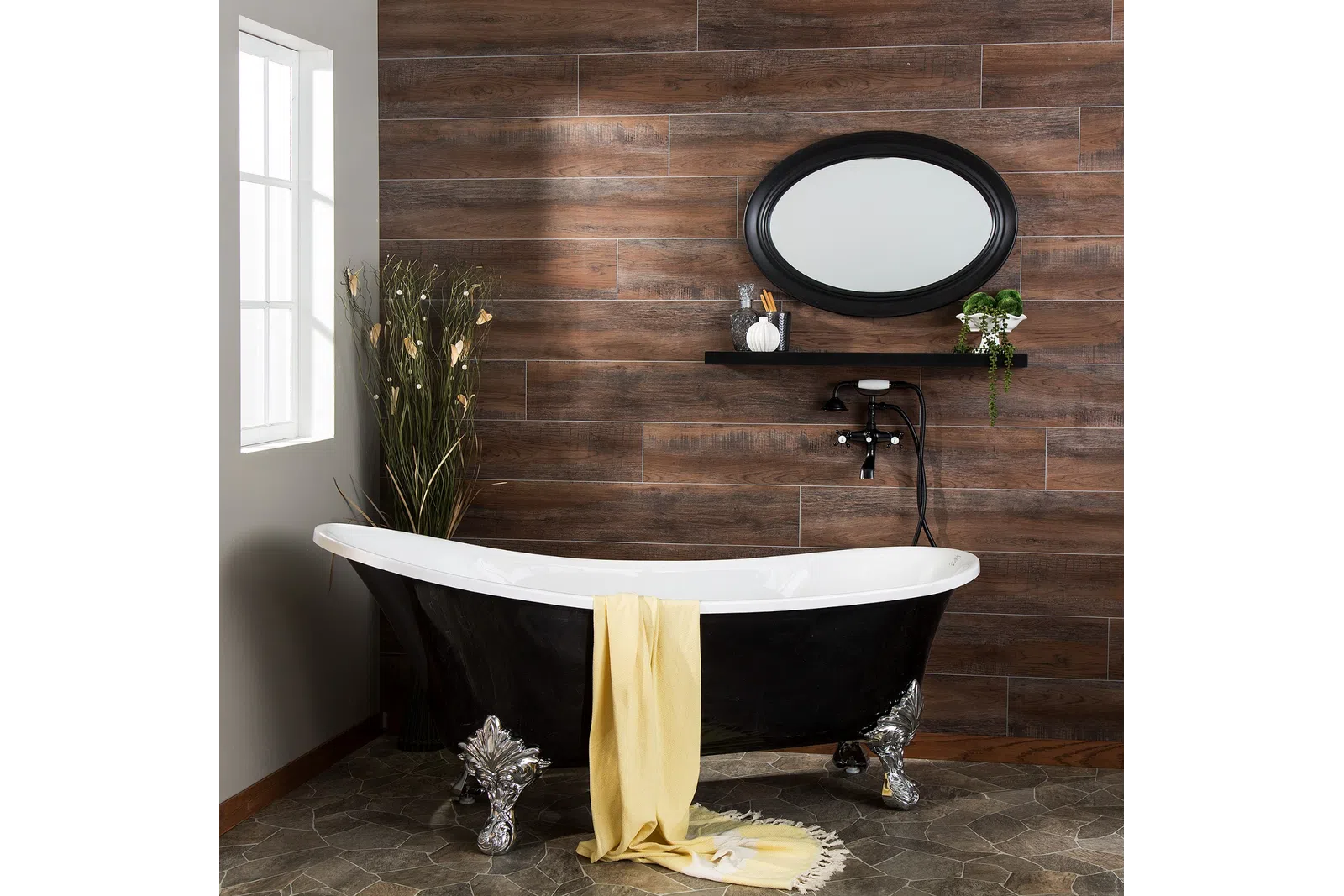 Black clawfoot bathtub with yellow towel in a rustic bathroom featuring wood wall tiles and oval mirror