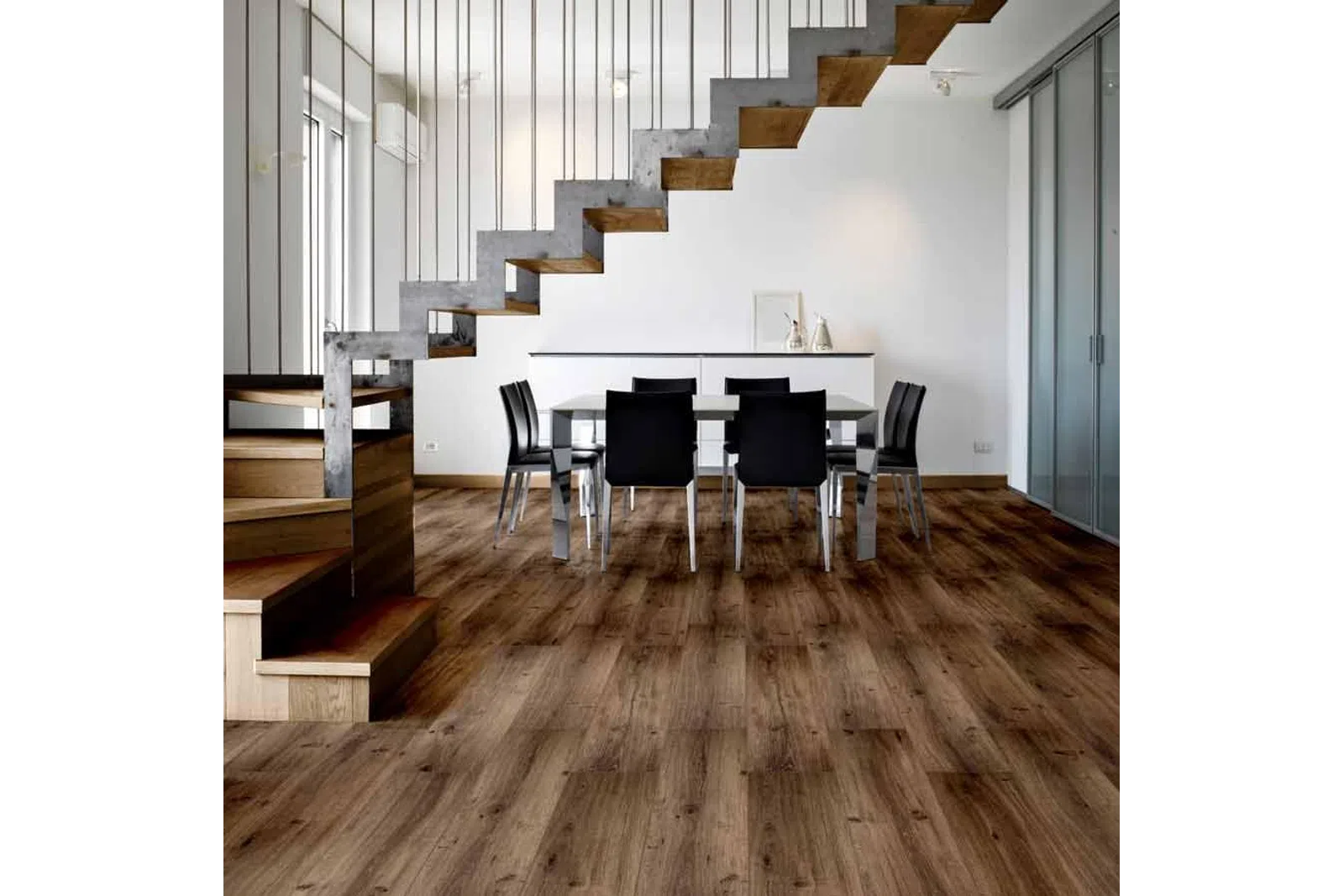 Modern dining room with wooden floors, black chairs, glass table, and industrial staircase with metal railings.