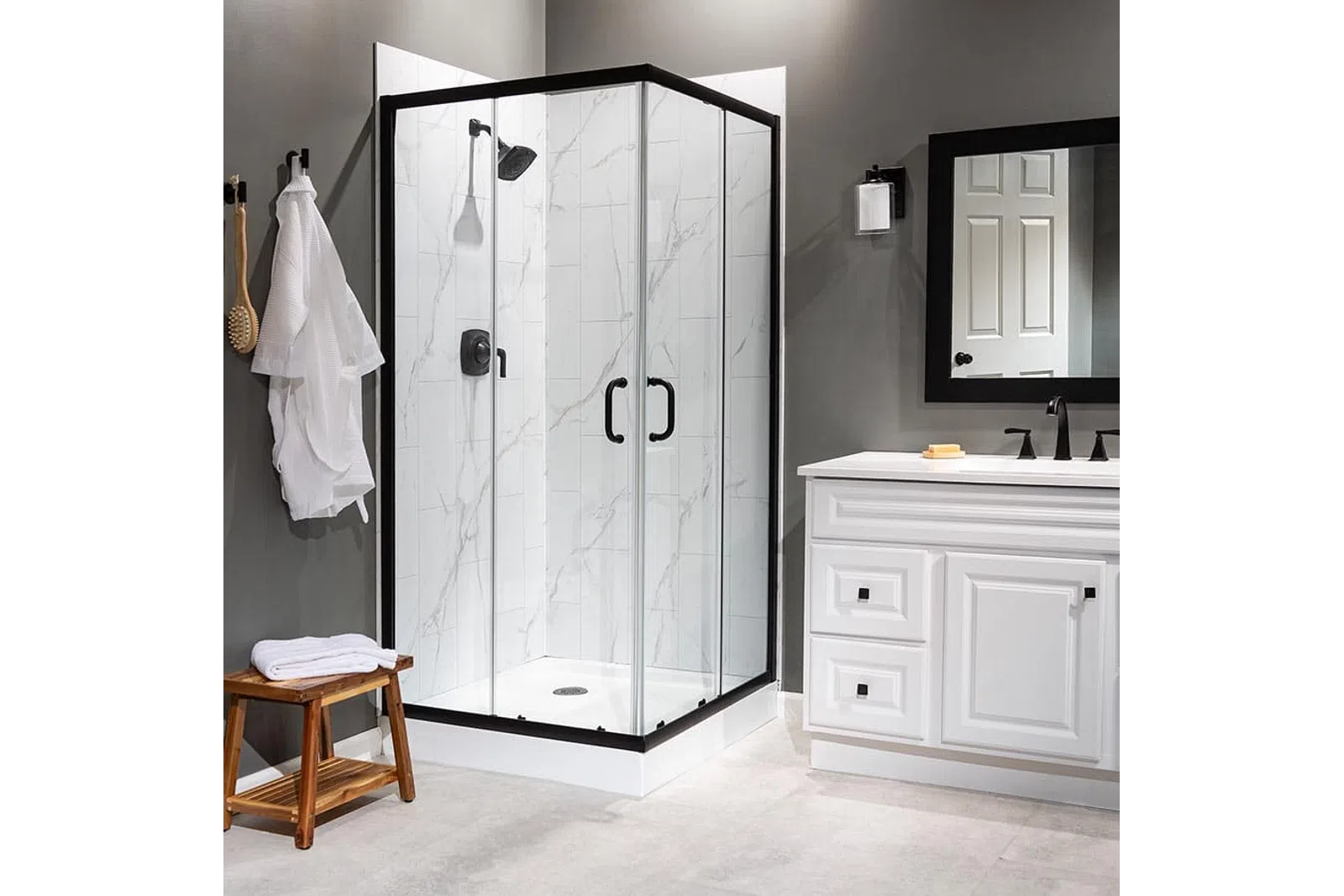 Modern bathroom with glass shower enclosure, white vanity, round mirror, and wooden bench with towels.