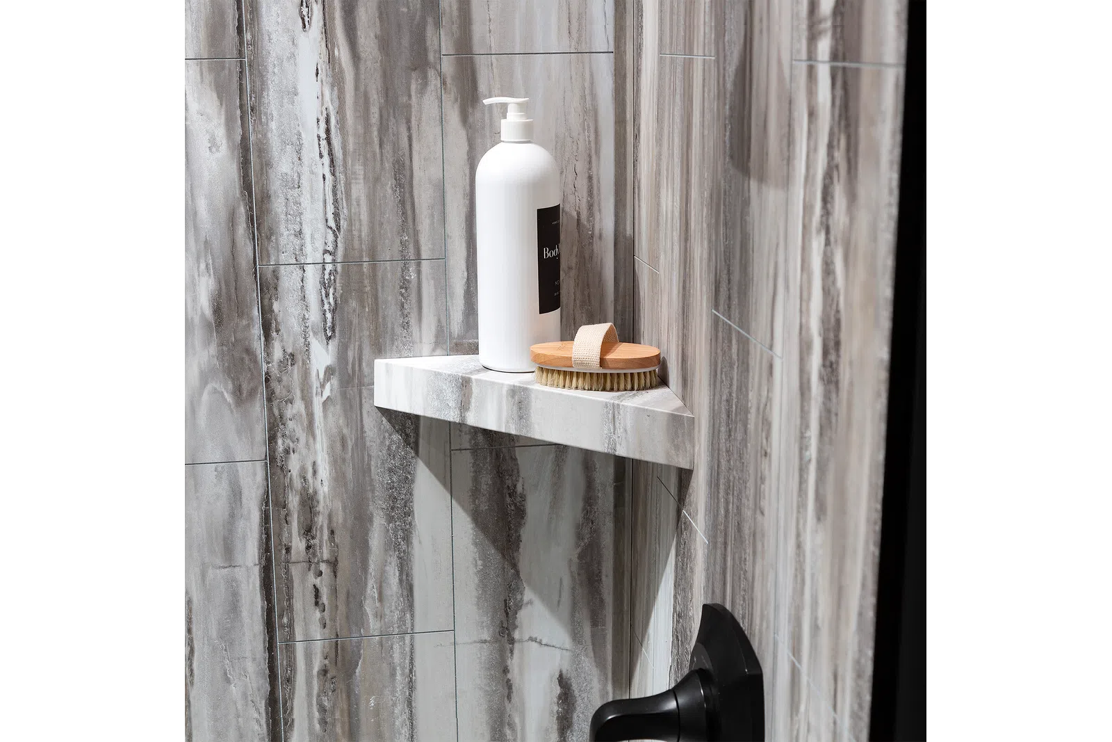 White pump bottle and wooden brush on marble corner shelf in gray tiled shower area