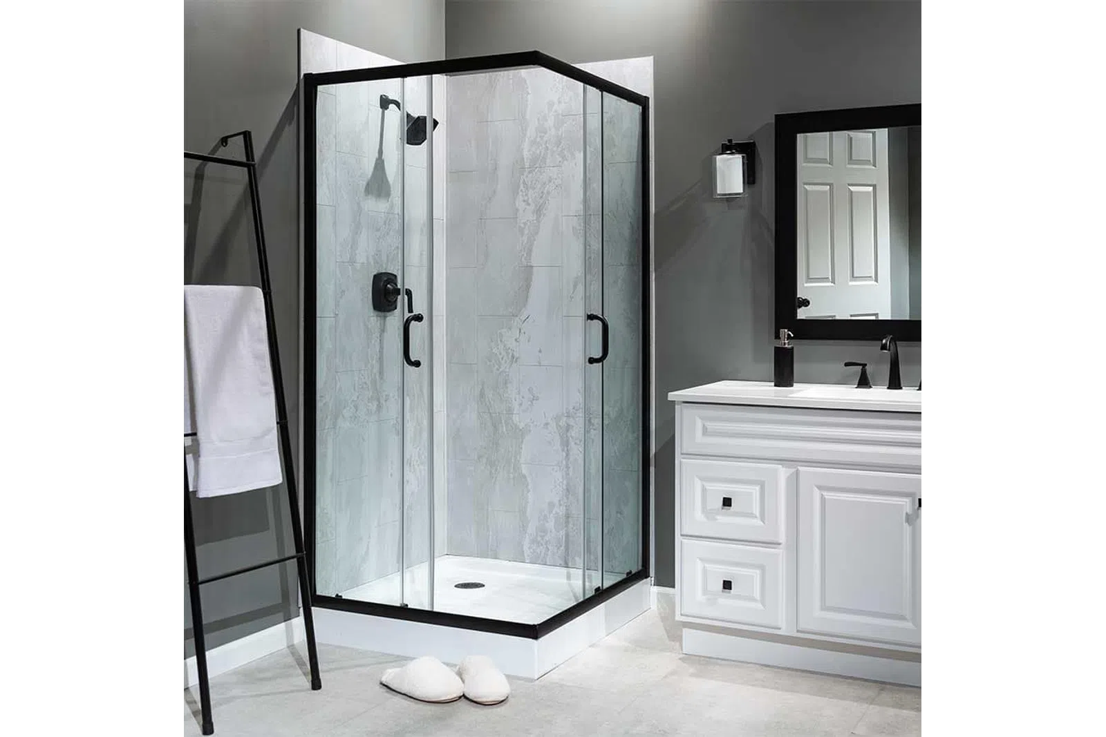 Modern corner glass shower with black frame, gray tile walls, white vanity, and towel rack in sleek bathroom