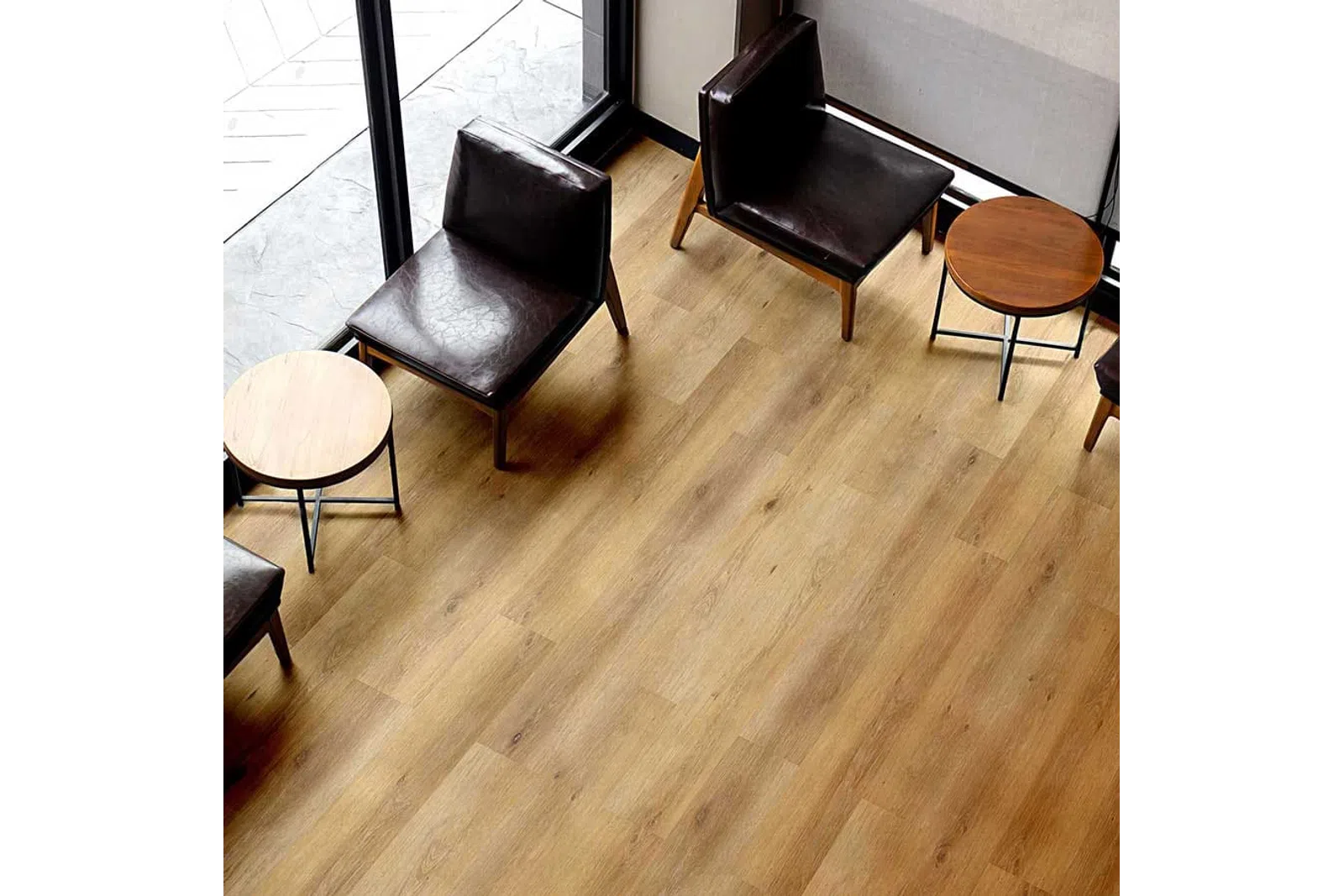 Modern seating area with dark leather chairs and round wooden tables on light hardwood floor near large windows.