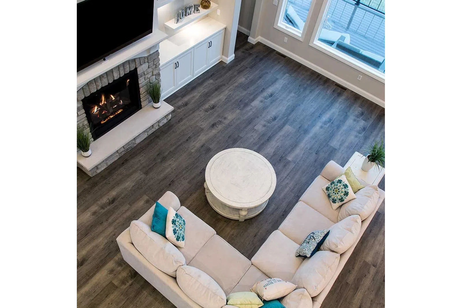 Cozy living room with beige sectional sofa, round white coffee table, dark wood floor, and lit stone fireplace.