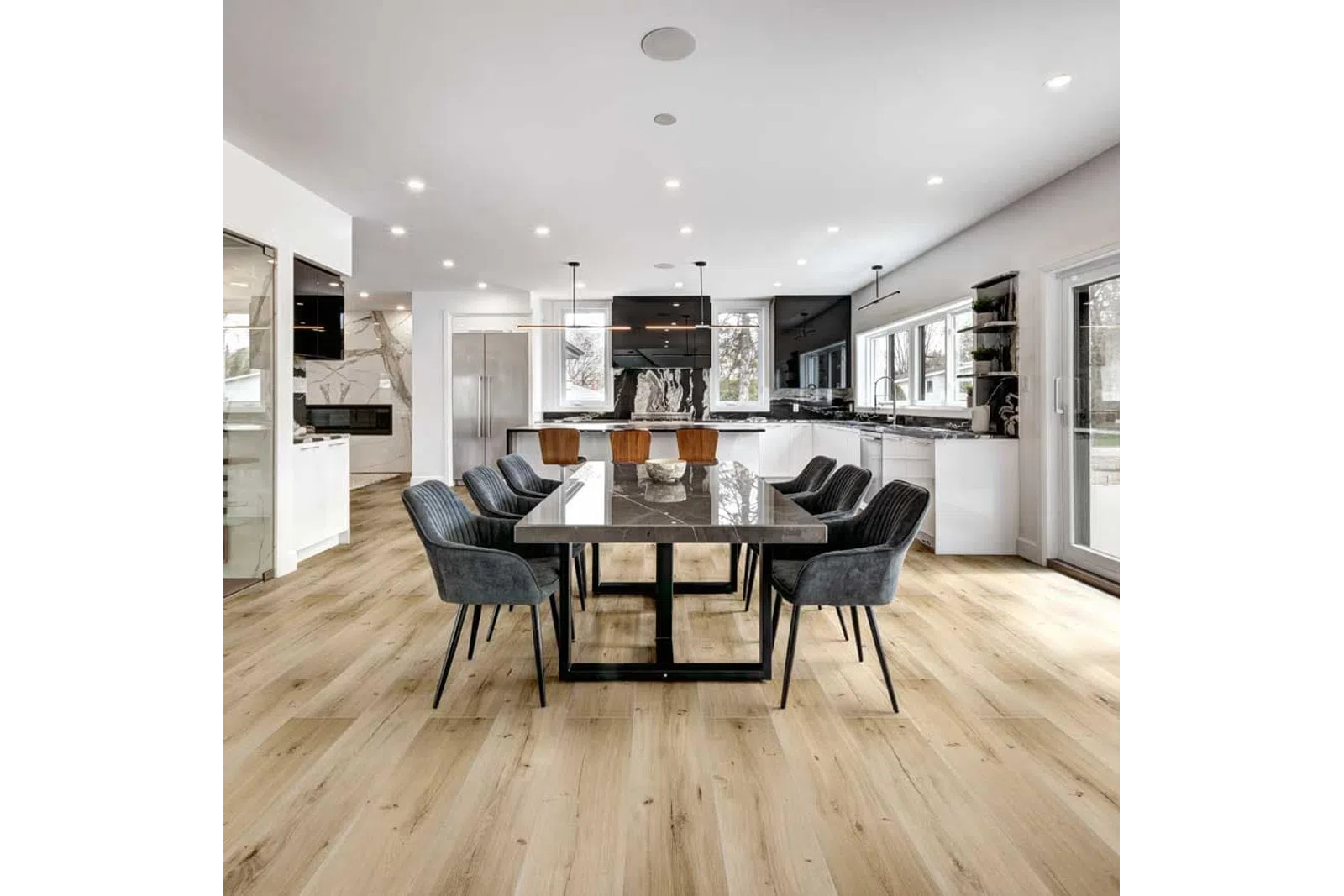 Spacious modern kitchen and dining area with black marble table, gray chairs, wood flooring, and large windows.