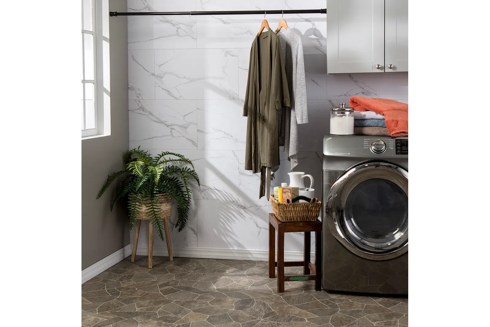 Modern laundry room with front-load washer, hanging robes, wicker plant stand, and folded clothes on cabinet