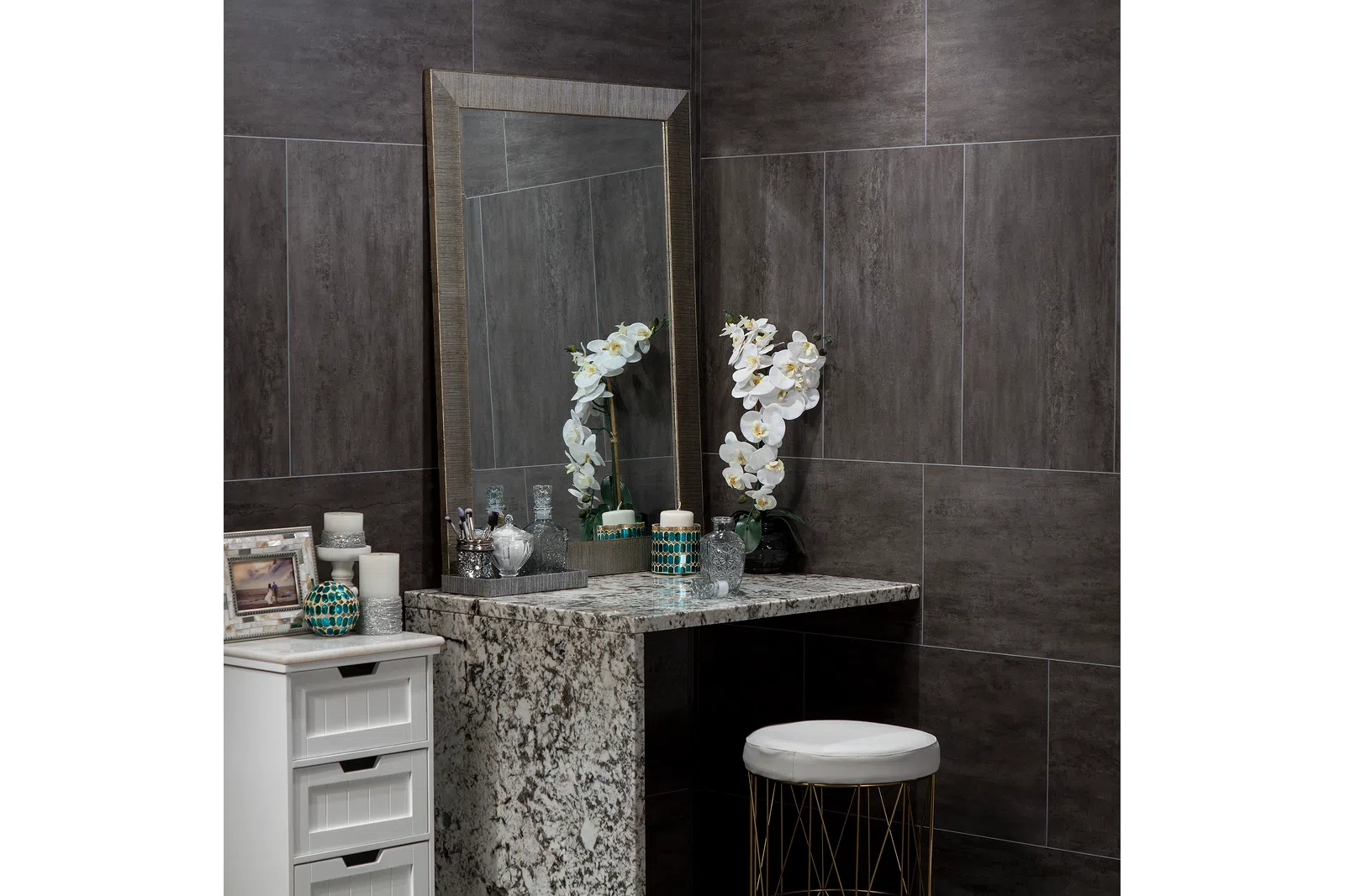 Modern vanity area with granite countertop, large mirror, white orchid, candles, and decorative items in gray tiled room