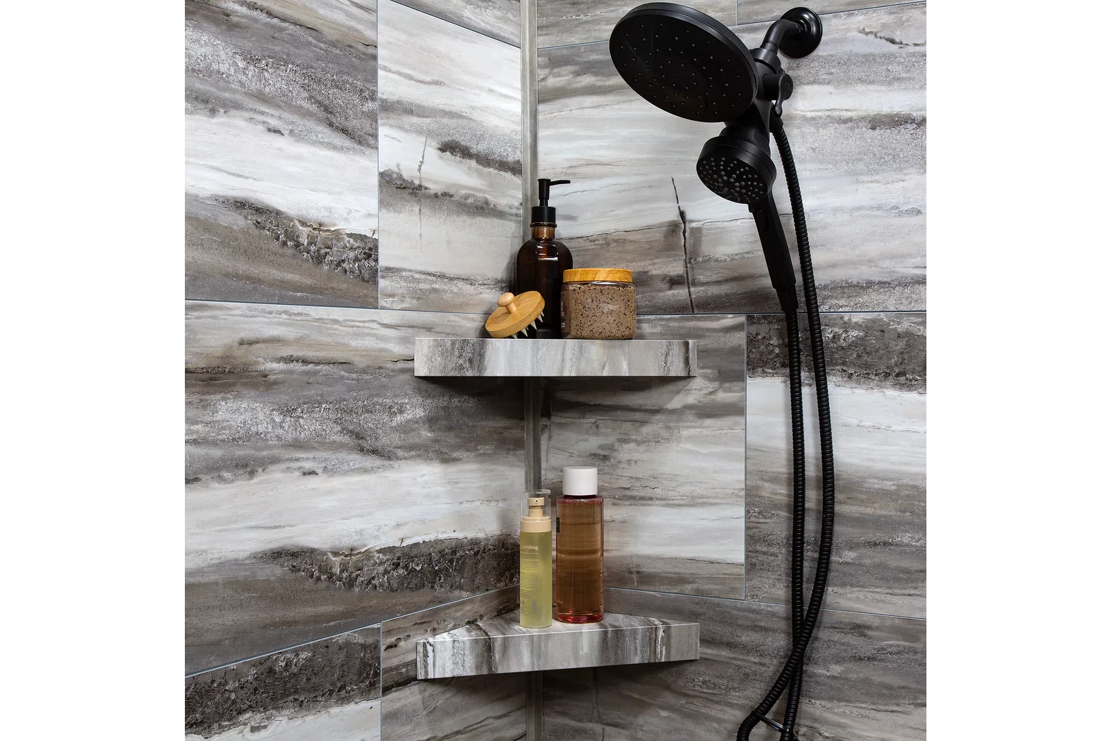 Modern shower corner with gray marble tiles, black showerhead, and shelves holding bath products and brush.
