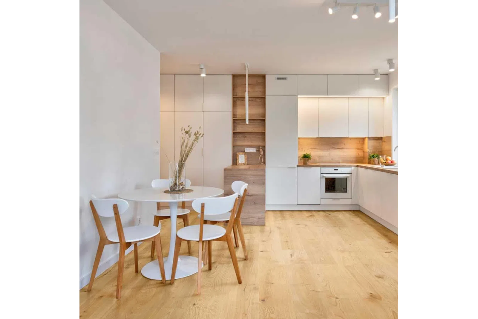Modern kitchen and dining area with white cabinets, wooden accents, round table, and wooden chairs on light hardwood floor