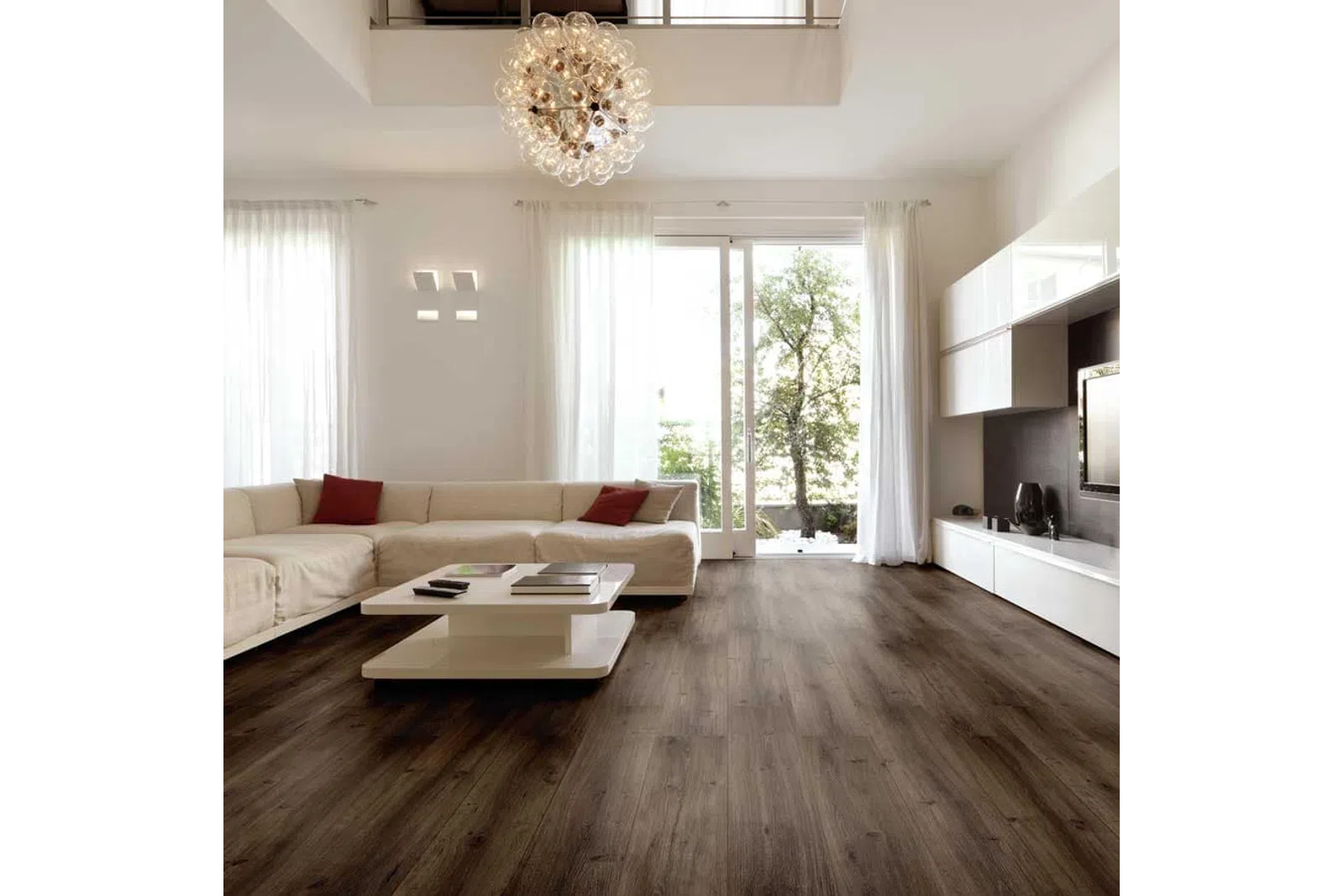 Modern living room with dark wood flooring, white sectional sofa, glass chandelier, and large windows with sheer curtains