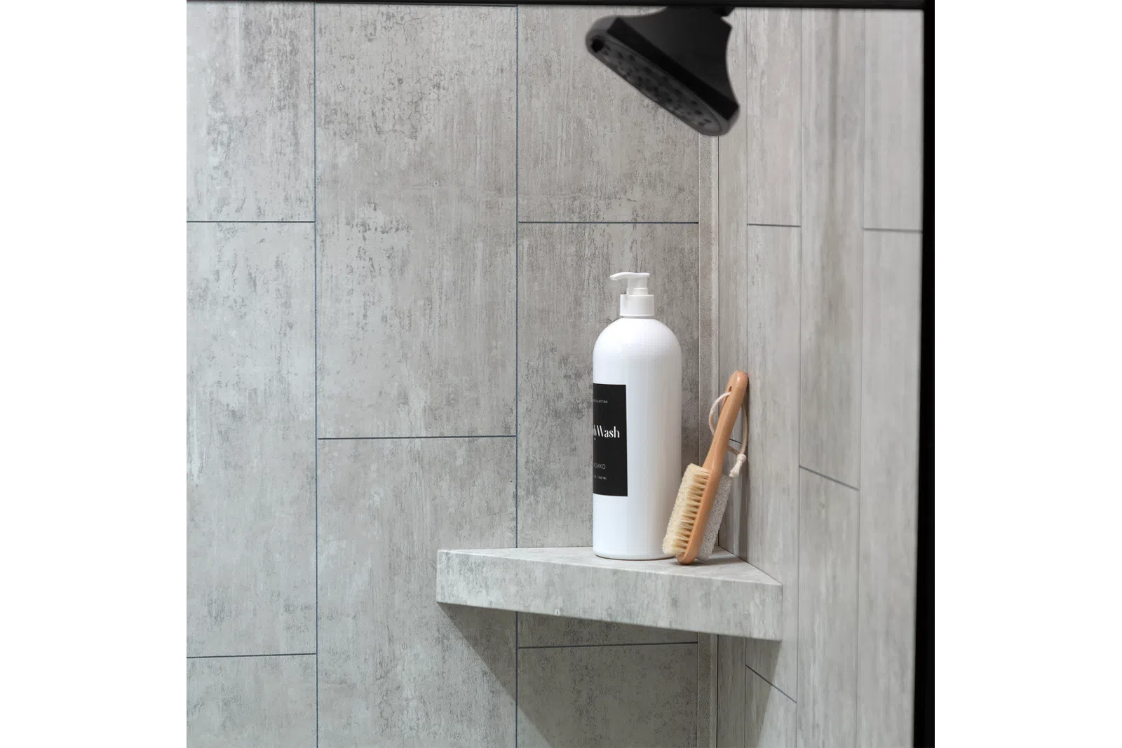 White pump bottle and wooden brush on corner shelf in modern gray tiled shower area under black showerhead.
