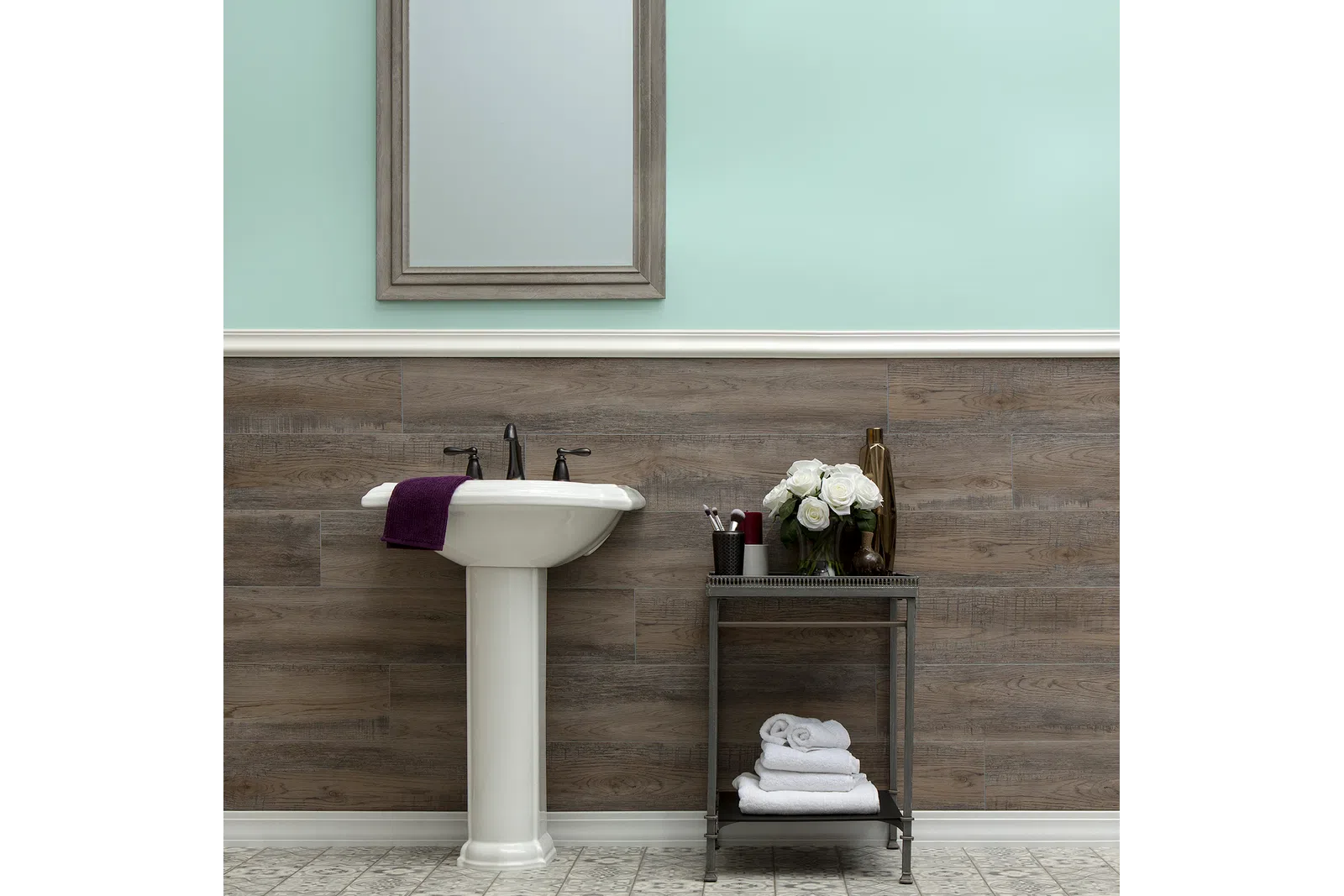 Modern bathroom with pedestal sink, wooden panel wall, light mint paint, mirror, and decorative towels and flowers.