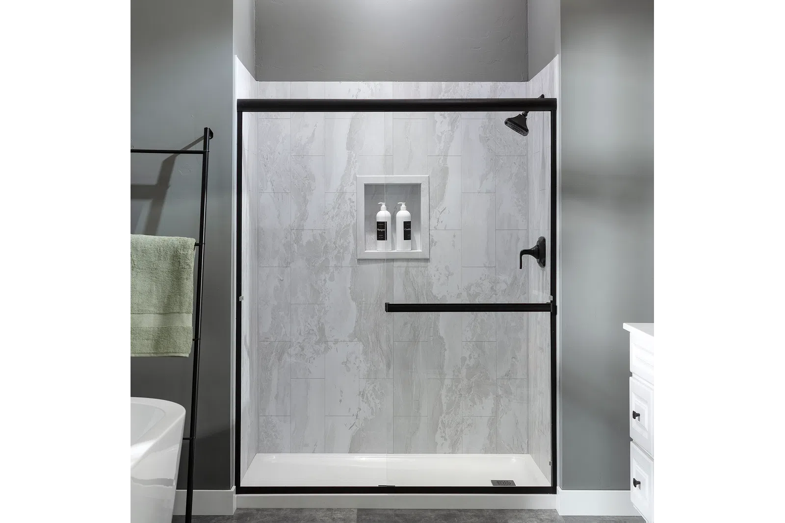 Modern bathroom shower with glass door, black fixtures, marble tiles, and built-in shelf with bottles.