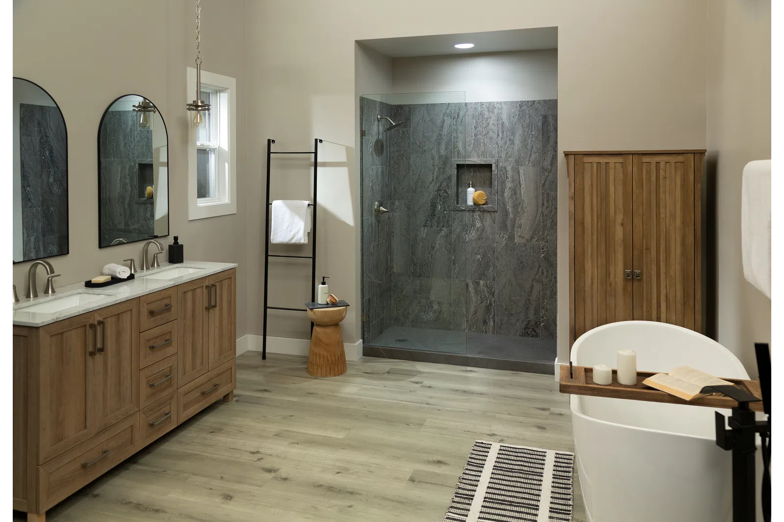 Modern bathroom with wood cabinetry, glass shower, freestanding tub, and light wood flooring.