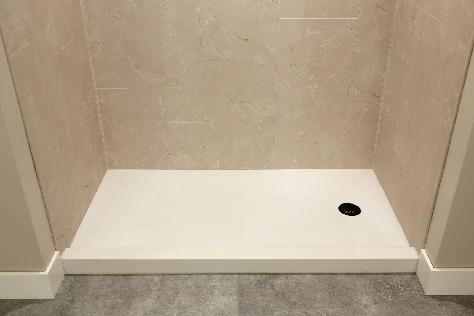 Empty white rectangular shower base with beige tiled walls and gray floor tile in a bathroom.
