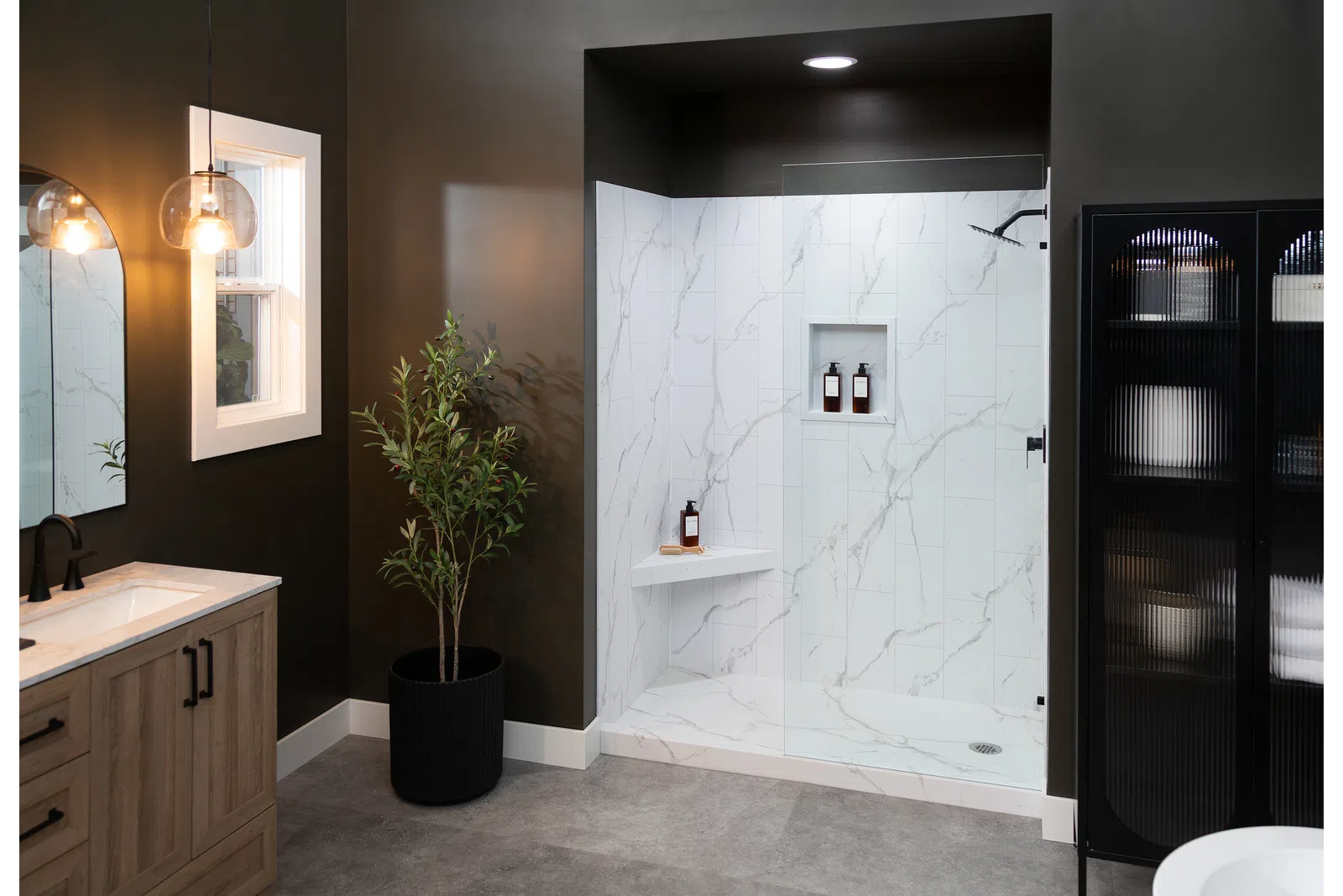 Modern bathroom with glass shower, marble tiles, wooden vanity, black cabinet, and indoor plant.