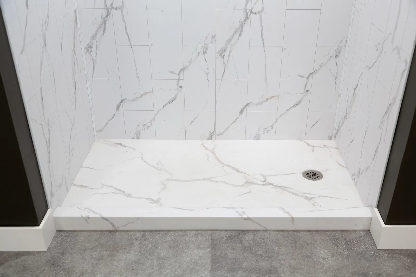 White marble shower area with veined tiles, a built-in drain, and gray textured floor outside the shower