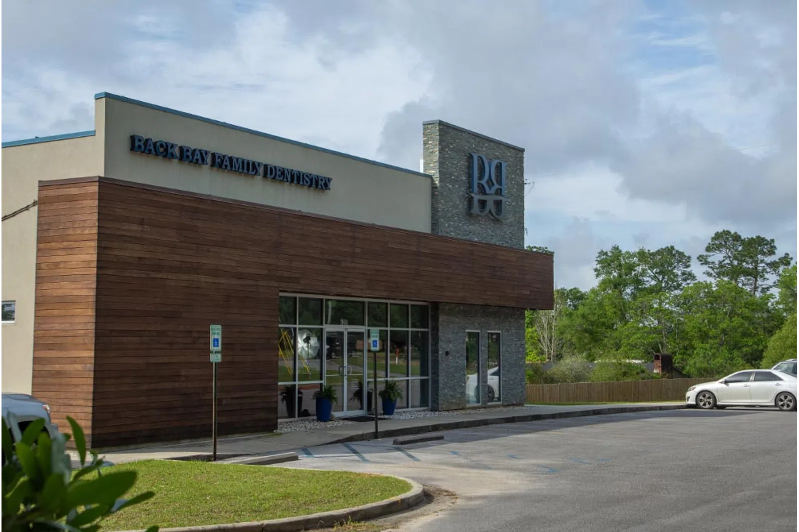 Modern Back Bay Family Dentistry building with wood and stone exterior and adjacent parking lot under a cloudy sky