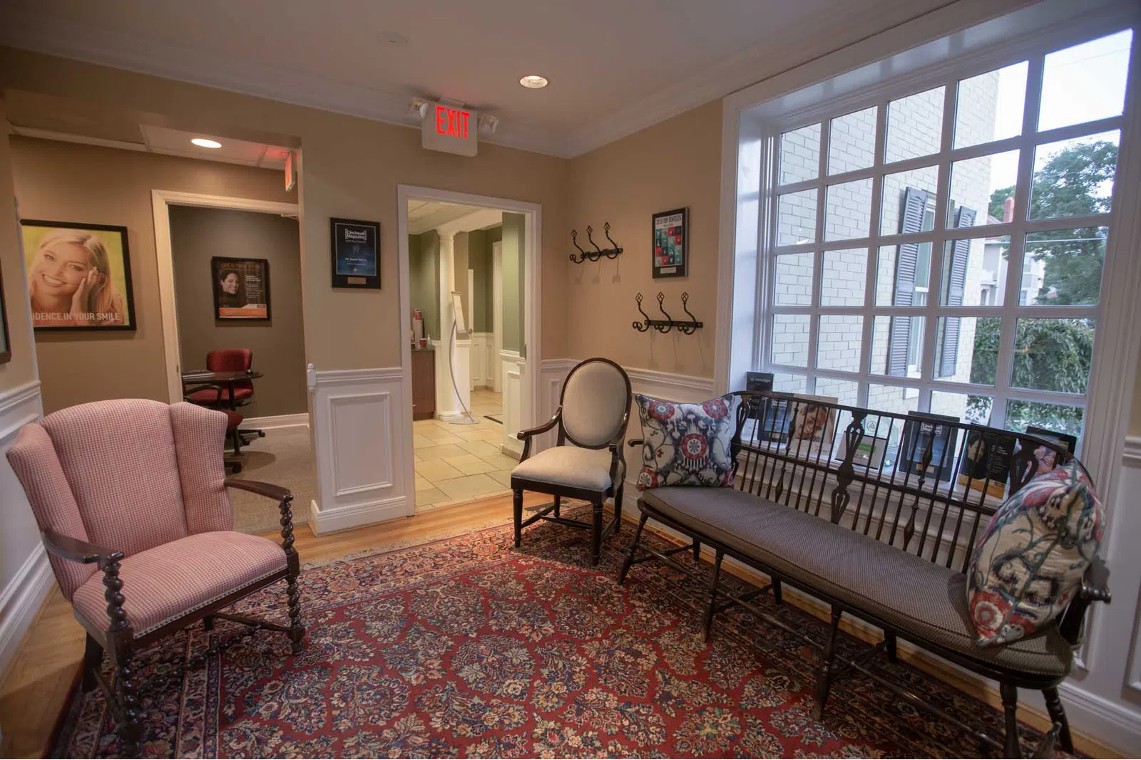 Cozy waiting room with vintage armchairs, a wooden bench with patterned cushions, and a large window letting in natural light.