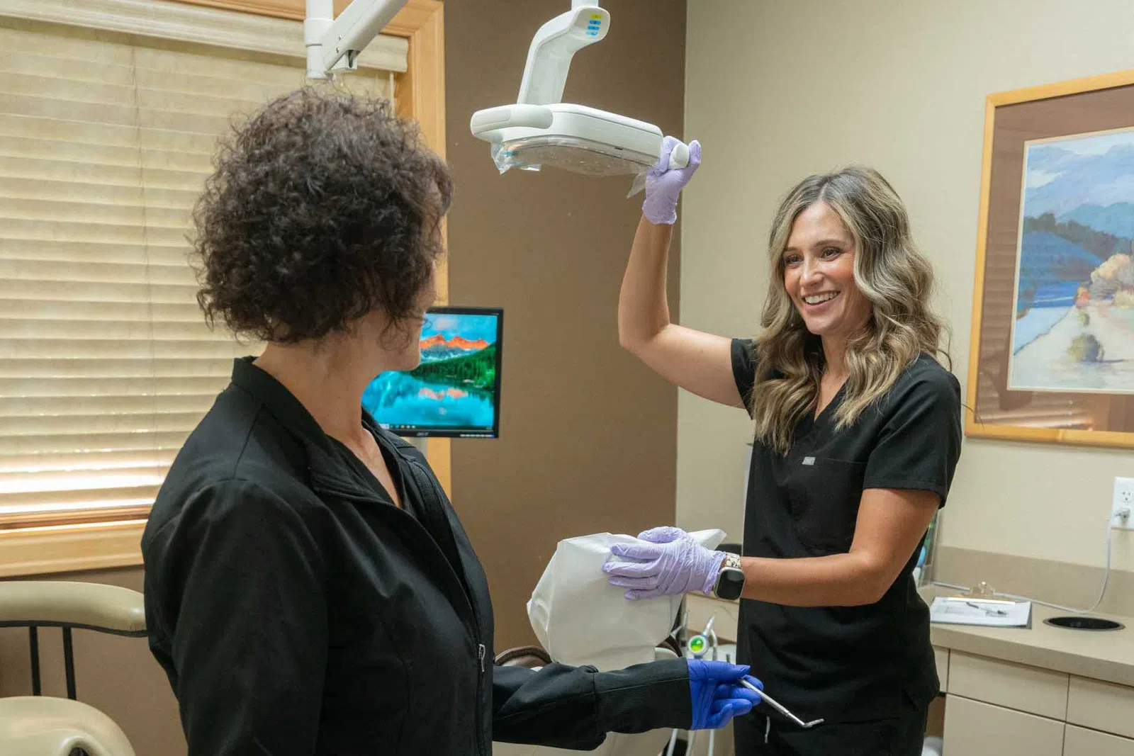 Female dentist adjusting dental light above patient in dental clinic during checkup appointment