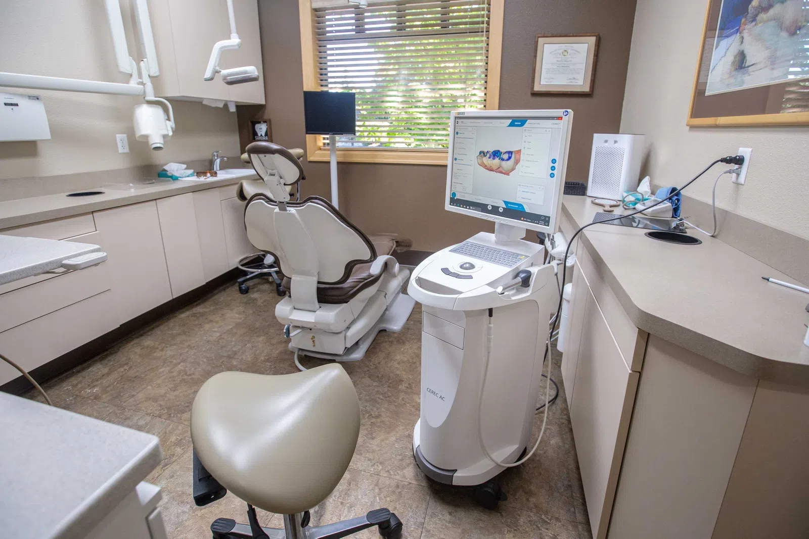 Modern dental office with patient chair, digital imaging equipment, and natural light from window blinds.