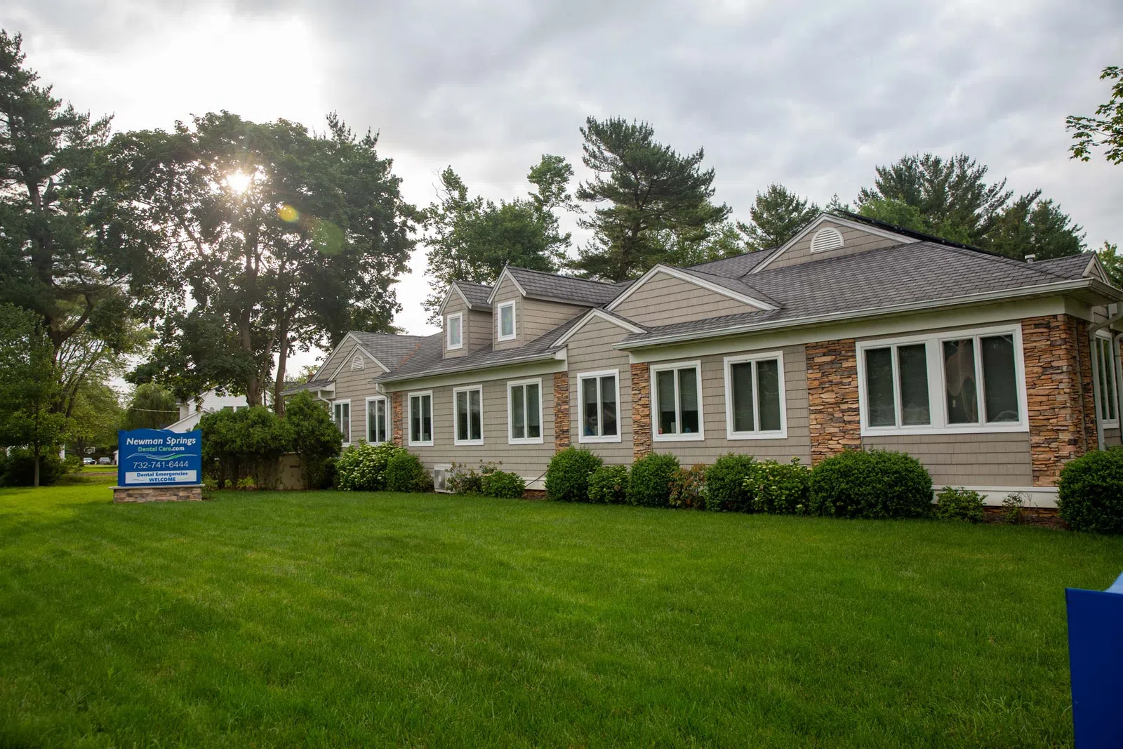 Modern single-story building with stone and siding exterior surrounded by green lawn and trees under cloudy sky.