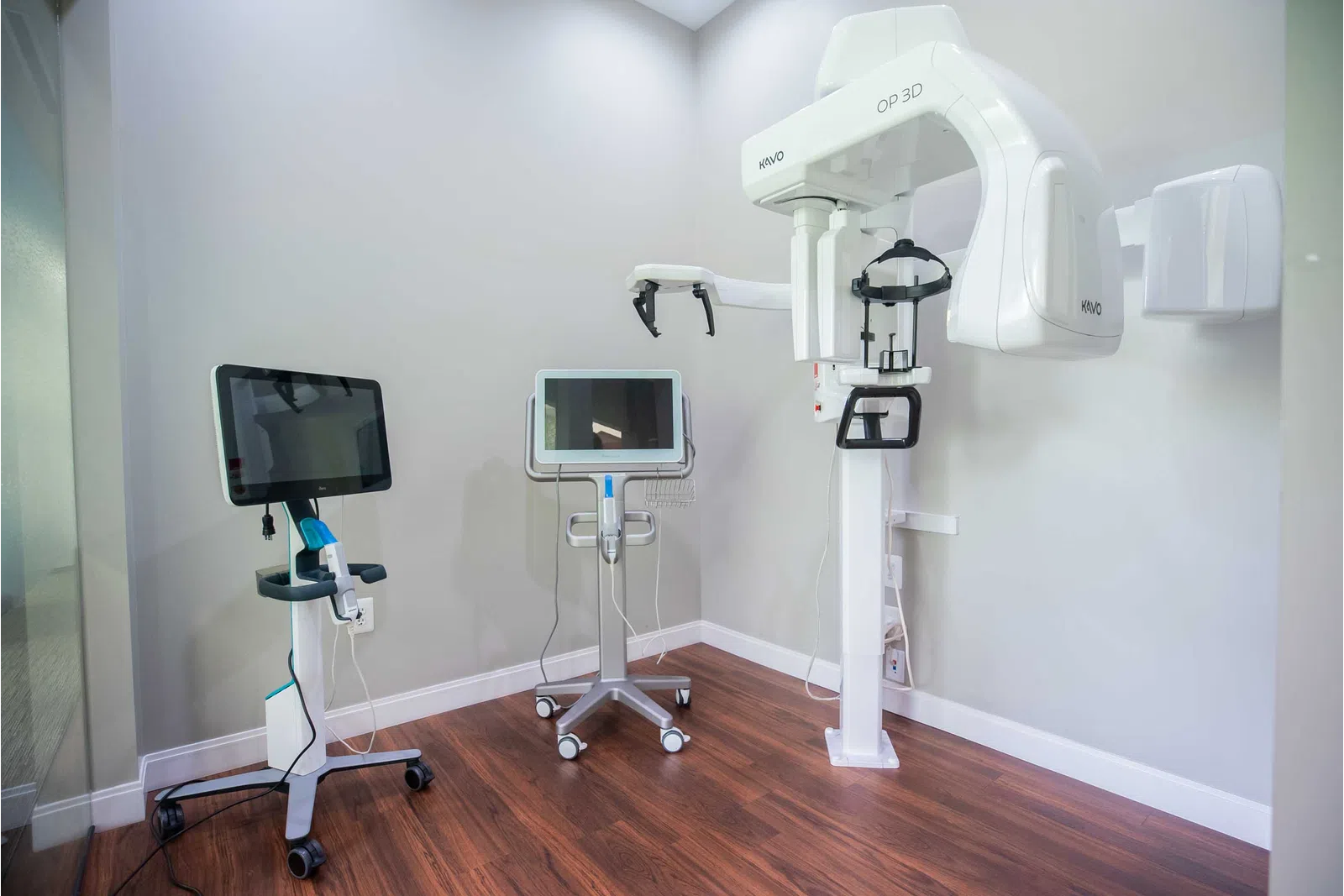 Dental imaging room with a 3D panoramic X-ray machine and two computer monitors on mobile stands.