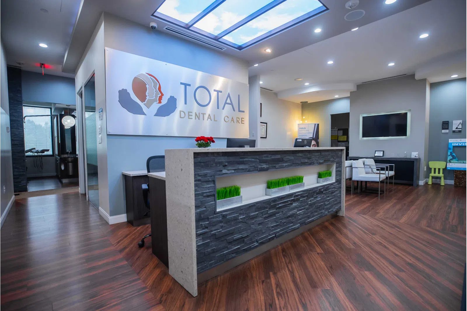 Modern dental office reception area with wood flooring, stone front desk, and Total Dental Care signage.
