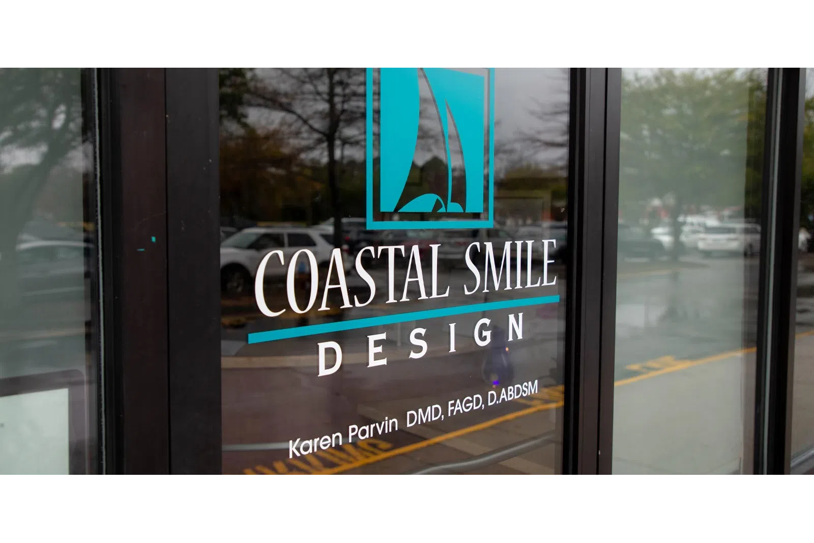 Coastal Smile Design logo with sailboat icon and dentist Karen Parvin's credentials on glass door.