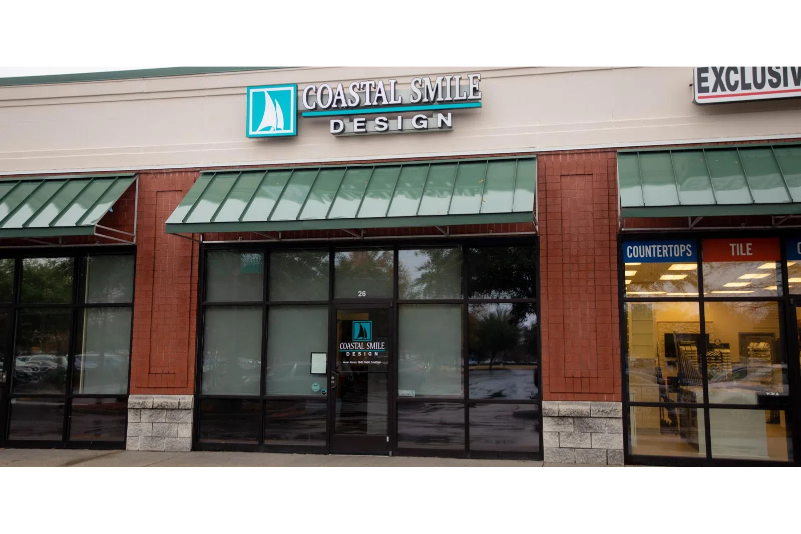 Storefront of Coastal Smile Design with teal sailboat logo and green awnings over glass windows and door
