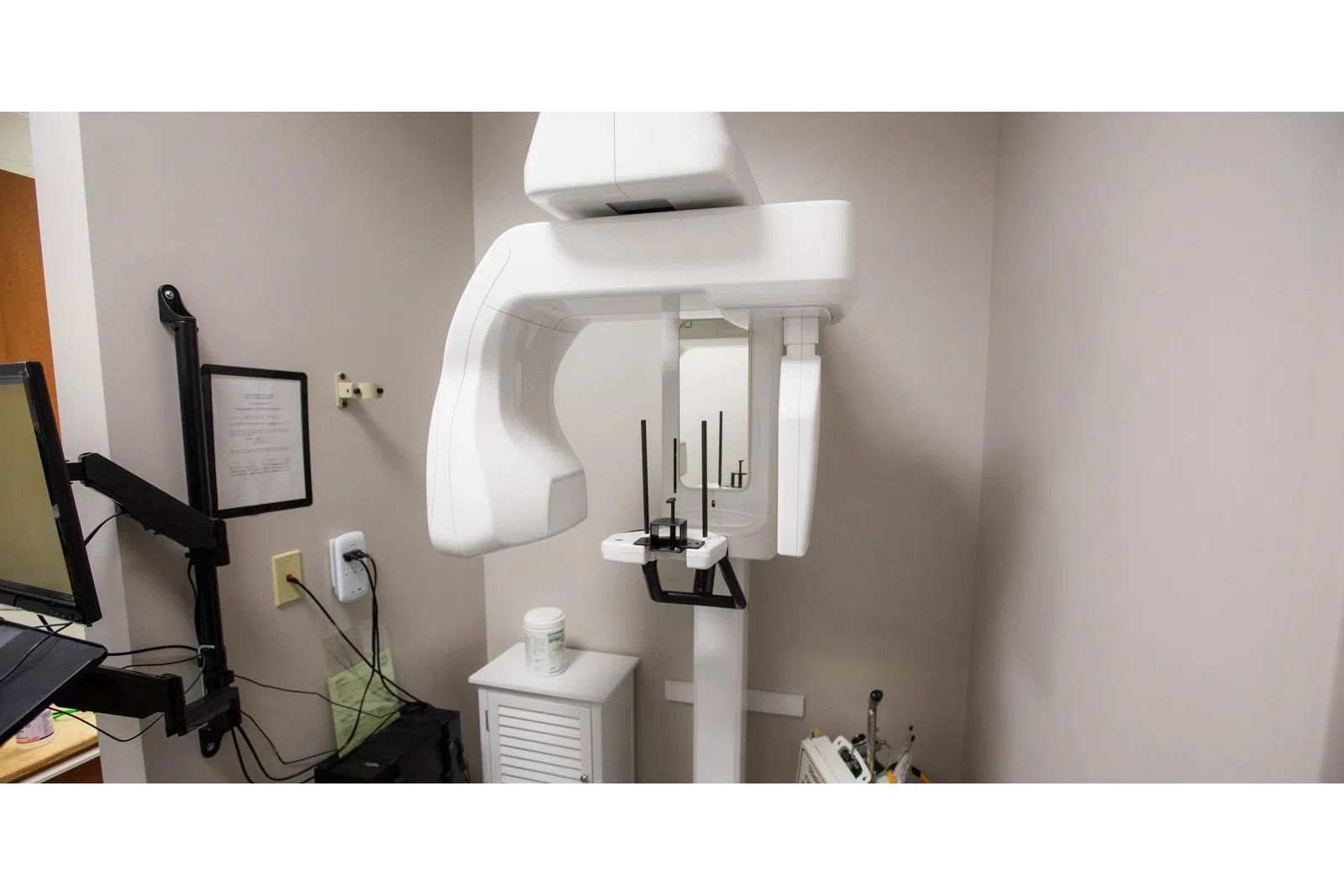 Modern dental X-ray machine in a clean clinic corner with computer setup and imaging equipment.